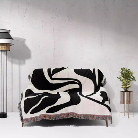Black and white Matisse flower woven throw blanket abstract patterned throw blanket on a couch against a light gray wall.