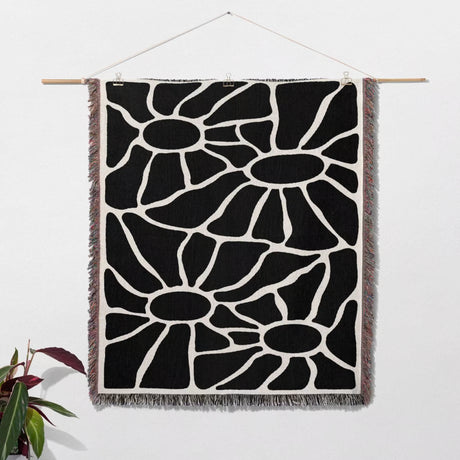 Black and white Matisse tapestry throw blanket for couch hanging on a white wall with a plant in the corner.