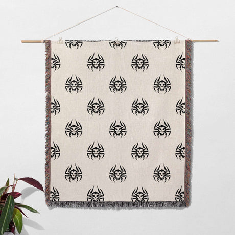 Woven blanket with black spider pattern on a beige background, hanging against a white wall.