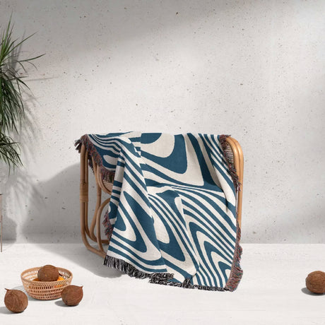 Blue cotton modern decorative woven throw blanket with abstract pattern draped over a chair against a light background