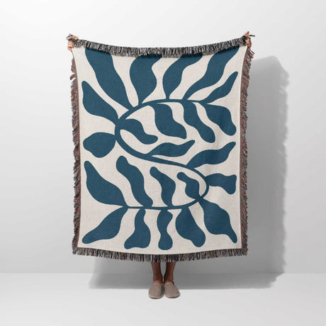 A person holding a blue leaf Matisse throw blanket on a white background