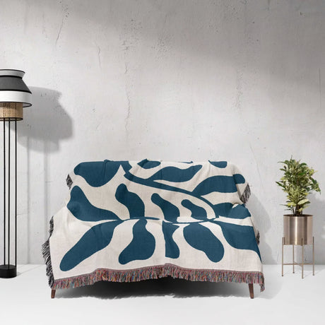 Blue leaf Matisse throw blanket on a couch against a white wall.