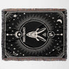 A horizontally laid out Capricorn Zodiac Blanket featuring a detailed design of the Capricorn symbol at the center. The blanket has a black background with white woven elements, including stars and celestial motifs around the central symbol, and multicolored fringe along the edges.