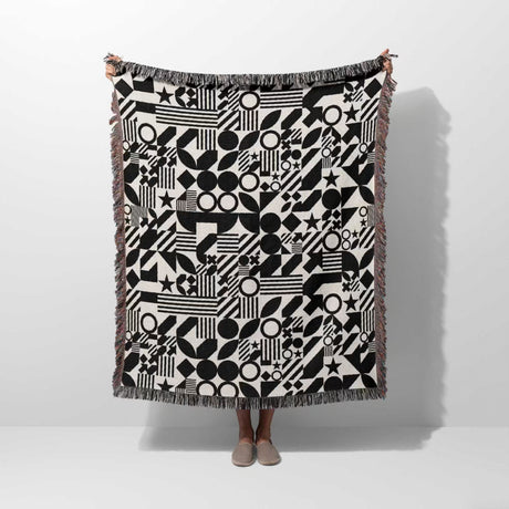 Black and white classical checker board pattern woven blanket throw held by a person on a white background.