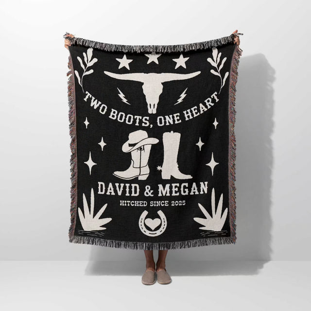 Cow skull and boots 2nd anniversary gift woven throw blanket with white text and graphics, including boots and a skull, held by a person on a white background.