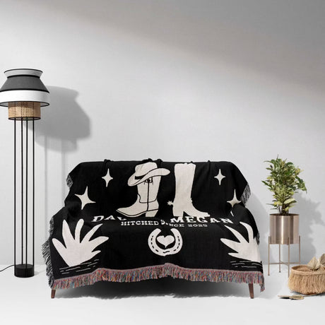 Cow skull and boots 2nd anniversary gift woven throw blanket with white designs draped over a couch in a room with a lamp and plant.