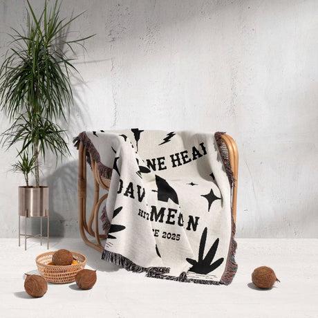 Cow skull and boots cotton anniversary gift woven throw blanket blanket with text draped over a chair next to a plant and coconuts on a light background