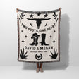 Cow skull and boots cotton anniversary gift woven throw blanket blanket with cowboy design and text on a white background held by a person. 