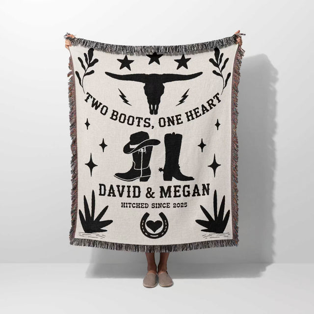 Cow skull and boots cotton anniversary gift woven throw blanket blanket with cowboy design and text on a white background held by a person. 