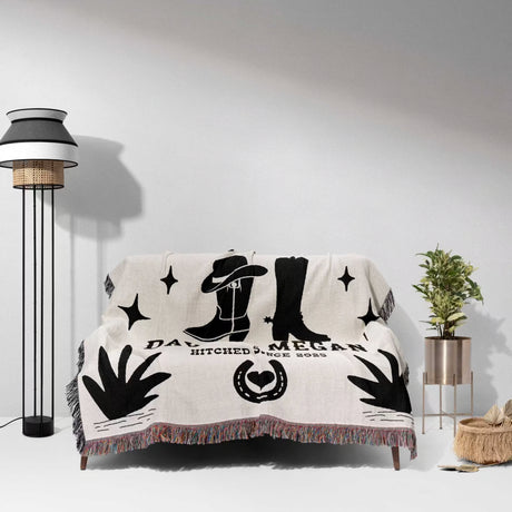 Cow skull and boots cotton anniversary gift woven throw blanket blanket with black designs on a white couch in a room with a lamp and plant.