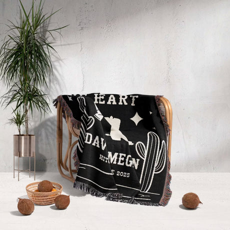 Cowboy boots wedding 2nd anniversary gift woven throw blanket with white text and graphics draped over a chair, with a plant and coconuts in the background.