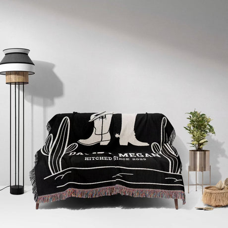 Cowboy boots wedding 2nd anniversary gift woven throw blanket with white designs and text draped over a sofa in a room with a lamp and plant.