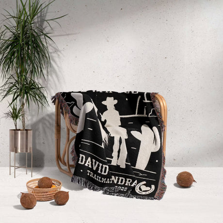 Cowboy and cowgirl 2nd anniversary gift woven throw blanket with white graphics and text draped over a chair, with a plant and decorative items in the background.