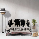 Cowboy and cowgirl cotton anniversary gift woven throw blanket with black animal silhouettes and text on a white couch against a light gray wall.