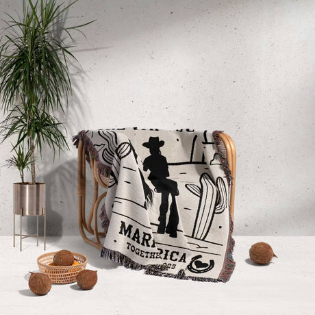 Cowboy and cowgirl couple cotton anniversary gift woven throw blanket  with cowboy design and custop text draped over a chair, with plants and decor items around.