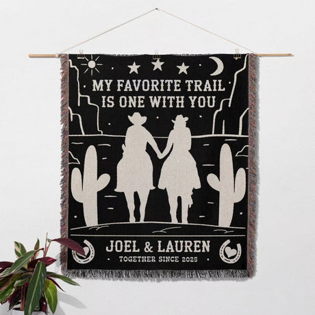 Cowboy and cowgirl on two horses 2nd anniversary gift woven throw blanket as a wall hanging with desert scene design, couple holding hands, and text 'My favorite trail is one with you' by Joel & Lauren.