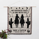 Cowboy and cowgirl on two horses cotton anniversary gift woven throw blanket with desert scene, couple holding hands, and text 'My favorite trail is one with you' by Paul & Caitlin.