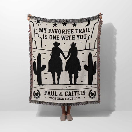 Cowboy and cowgirl on two horses cotton anniversary gift woven throw blanket held by a person with cowboy design and text 'My favorite trail is one with you' by Paul & Caitlin