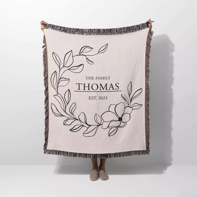Custom family name cotton throw blanket with floral design and text 'The Family Thomas Est. 2023' on a white background