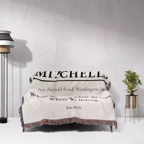 Custom family name and address blanket with text draped over a couch against a white wall