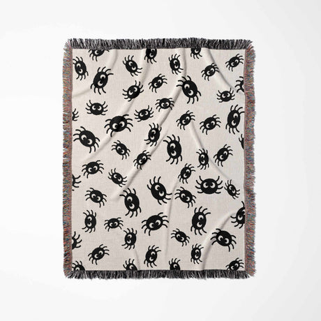 The Cute Halloween Blanket is laid out vertically, emphasizing its size and design. The image shows a full view of the blanket, adorned with charming black spiders scattered across an off-white background. The multicolored fringe along the border adds a delightful splash of color to the playful spider design.