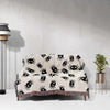 This image showcases the Cute Halloween Blanket spread out over a couch, demonstrating its perfect fit for adding a touch of Halloween charm to any seating area. The blanket’s design, featuring cute black spiders on an off-white background, paired with the vibrant multicolored fringe, makes it an ideal decorative and functional piece.