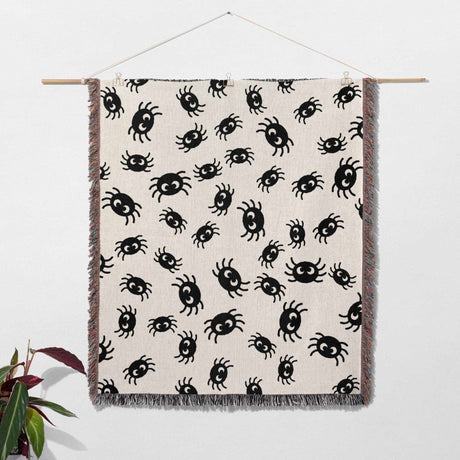 Cute spiders woven throw blanket for Halloween décor on a beige background, hanging against a white wall.