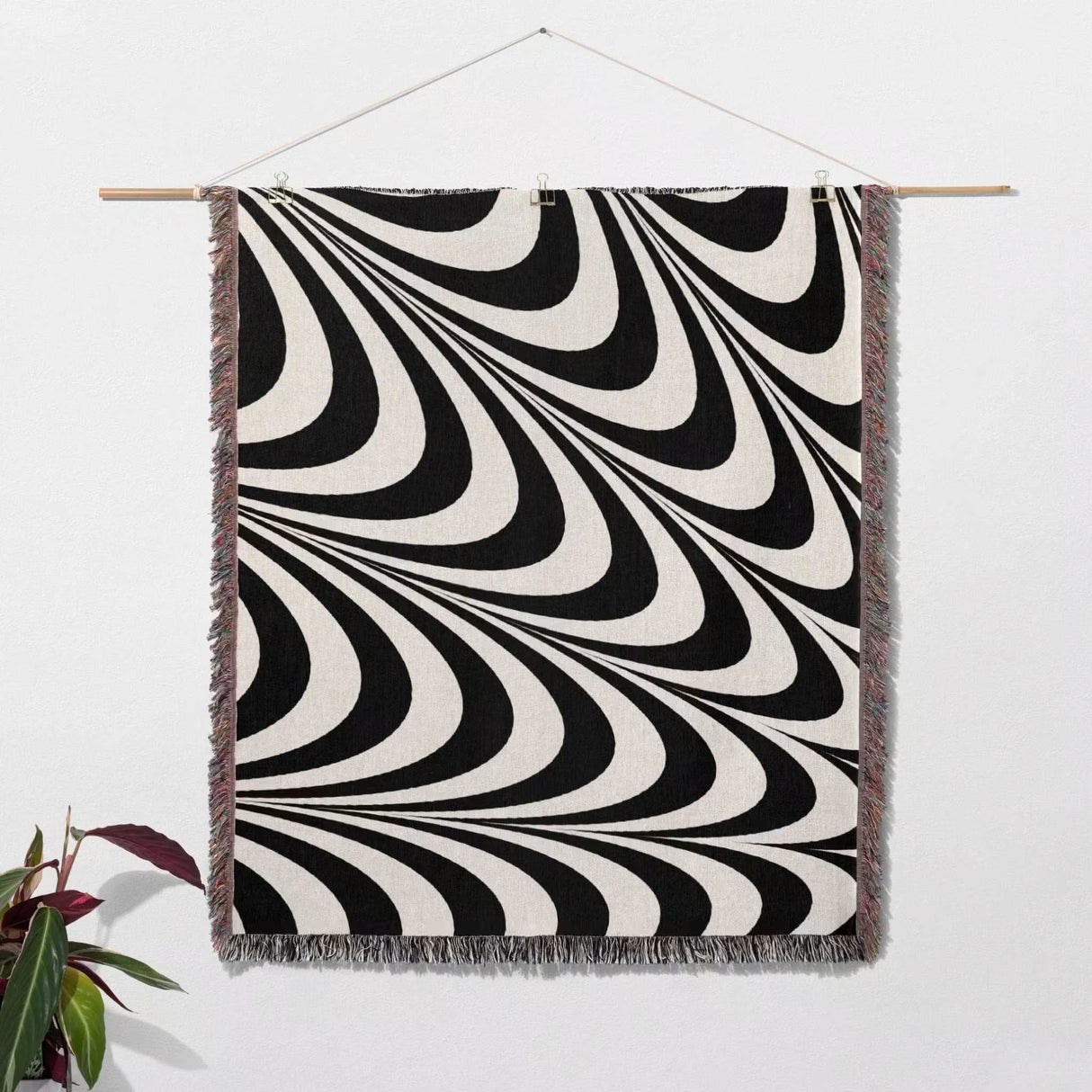 Black and white decorative abstract waves woven blanket throw tapestry with fringe hanging on a wooden rod against a white wall.