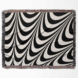 Black and white decorative abstract waves woven blanket throw tapestry with fringed edges flat lay on a white background.