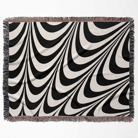 Black and white decorative abstract waves woven blanket throw tapestry with fringed edges flat lay on a white background.