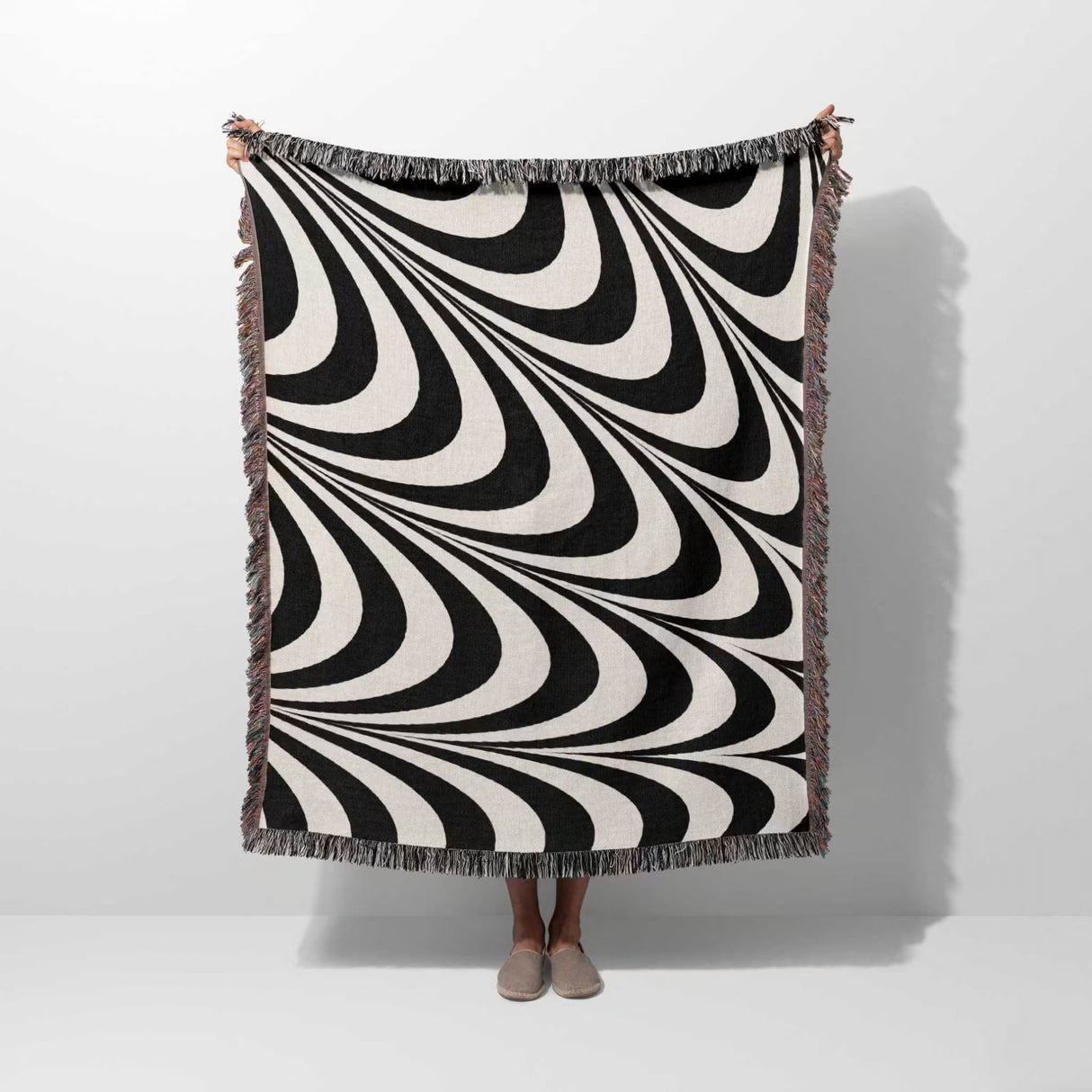 Black and white decorative abstract waves woven blanket throw tapestry draped over a person on a white background.
