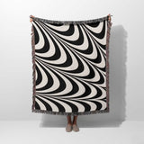 Black and white decorative abstract waves woven blanket throw tapestry draped over a person on a white background.