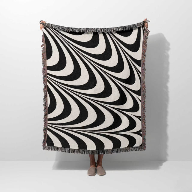Black and white decorative abstract waves woven blanket throw tapestry draped over a person on a white background.