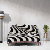 Black and white decorative abstract waves woven blanket throw tapestry on a couch against a light gray wall.