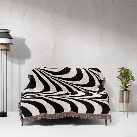 Black and white decorative abstract waves woven blanket throw tapestry on a couch against a light gray wall.