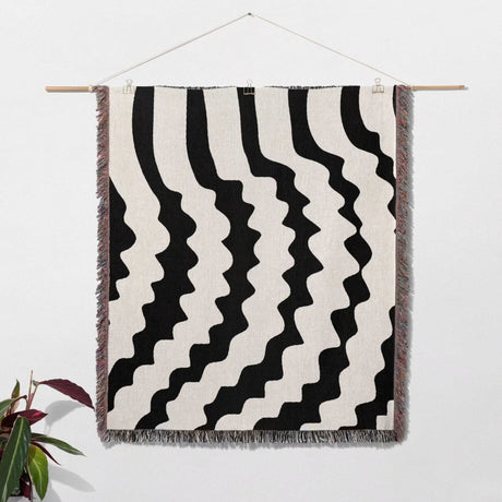 Black and white decorative abstract wavy woven blanket throw hanging on a wall.