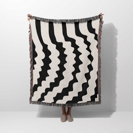 Black and white decorative abstract wavy woven blanket throw held by a person on a white background