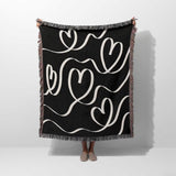 Black and white decorative hearts woven blanket throw held by a person on a white background