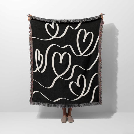 Black and white decorative hearts woven blanket throw held by a person on a white background