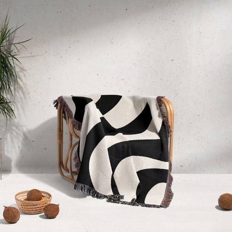 Black and white decorative modern woven blanket throw tapestry draped over a wicker chair against a light gray wall.