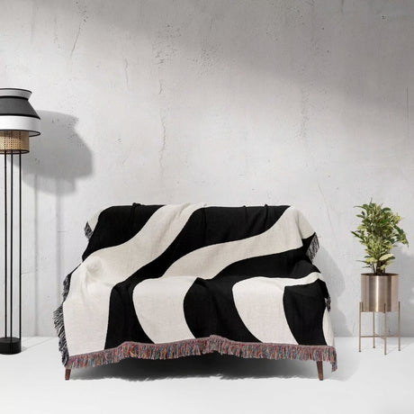 Black and white decorative modern woven blanket throw tapestry draped over a sofa against a light gray wall.