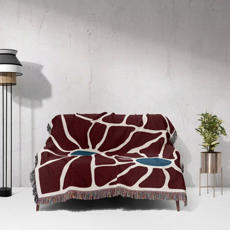 Decorative eclectic Matisse inspired tapestry throw blanket for couch with a unique pattern draped over a couch against a white wall.