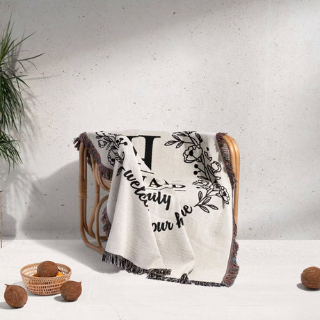 Family monogrammed woven throw blanket for couch and bed with decorative text and patterns draped over a chair against a light background