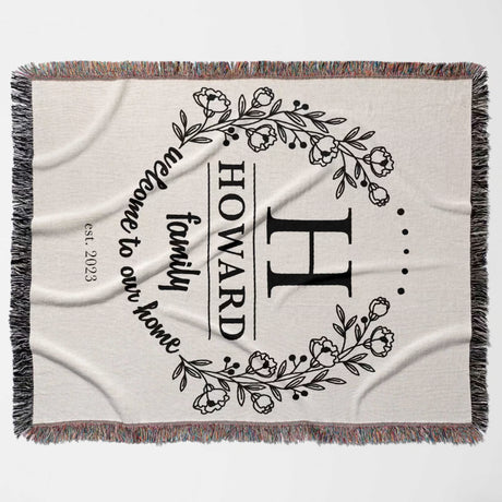 Family monogrammed woven throw blanket for couch and bed with decorative text and floral design flat lay on a white background