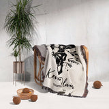 Floral cow skull cotton anniversary gift woven throw blanket with black floral design and text draped over a chair in a room with a plant and decorative items.