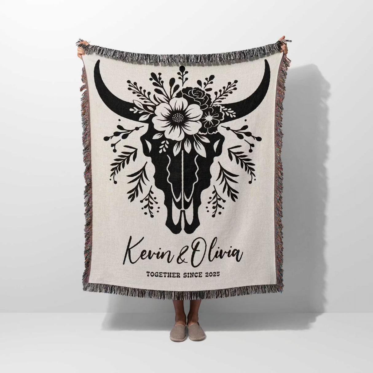 Floral cow skull cotton anniversary gift woven throw blanket held by a person with bull skull design and personalized text on a white background