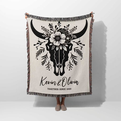 Floral cow skull cotton anniversary gift woven throw blanket held by a person with bull skull design and personalized text on a white background