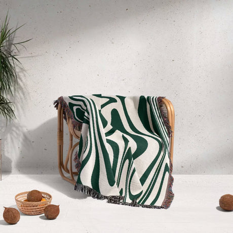 Forest green marble woven throw blanket for couch draped over a chair against a light gray wall.