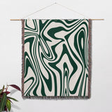 Forest green marble woven throw blanket for couch with green and white abstract marble pattern hanging on a white wall.