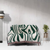 Sofa with an abstract patterned forest green marble woven throw blanket for couch against a white wall.